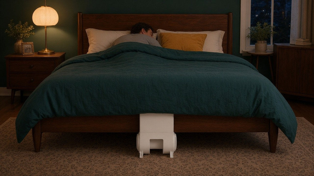 Evening bedroom with a man asleep and a bFan centered at the foot of the bed, the setup good bed fan reviews describe