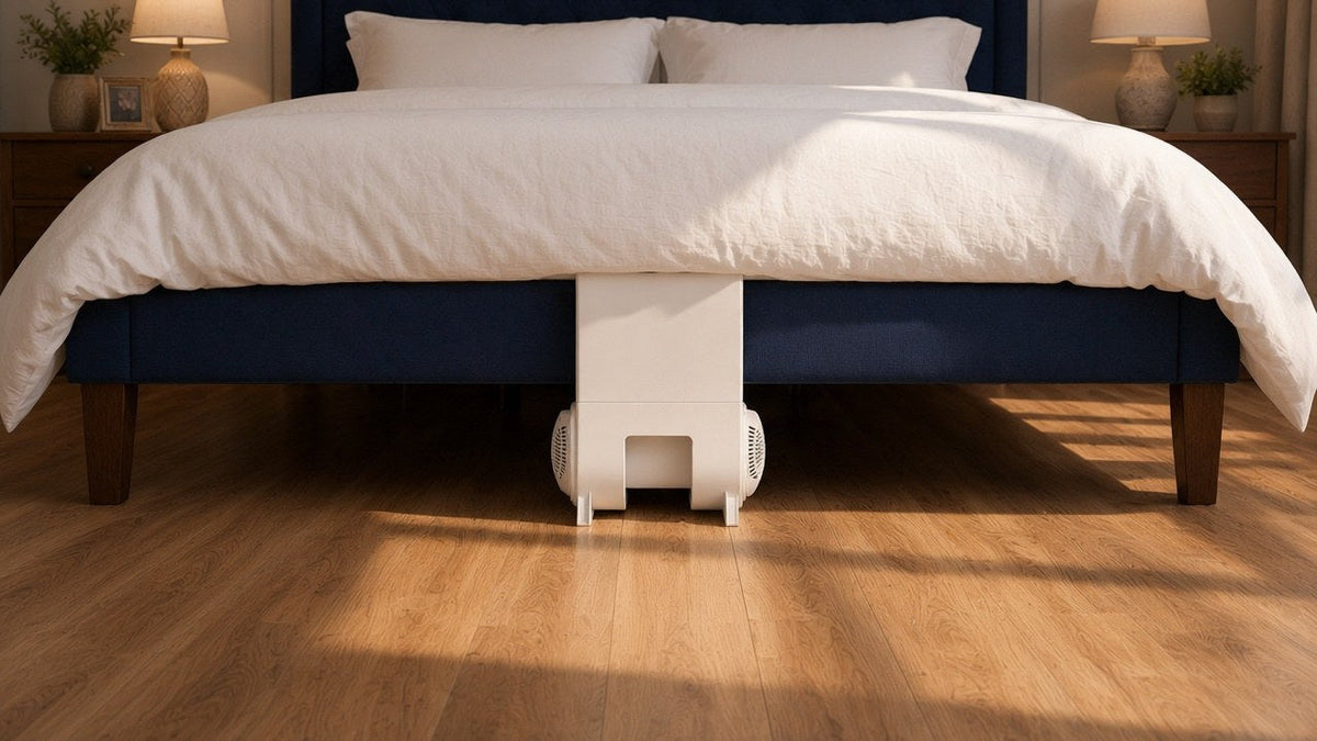 Foot of a navy bed with a bFan under bed fan base centered on the floor and its upright panel tucked under a white duvet